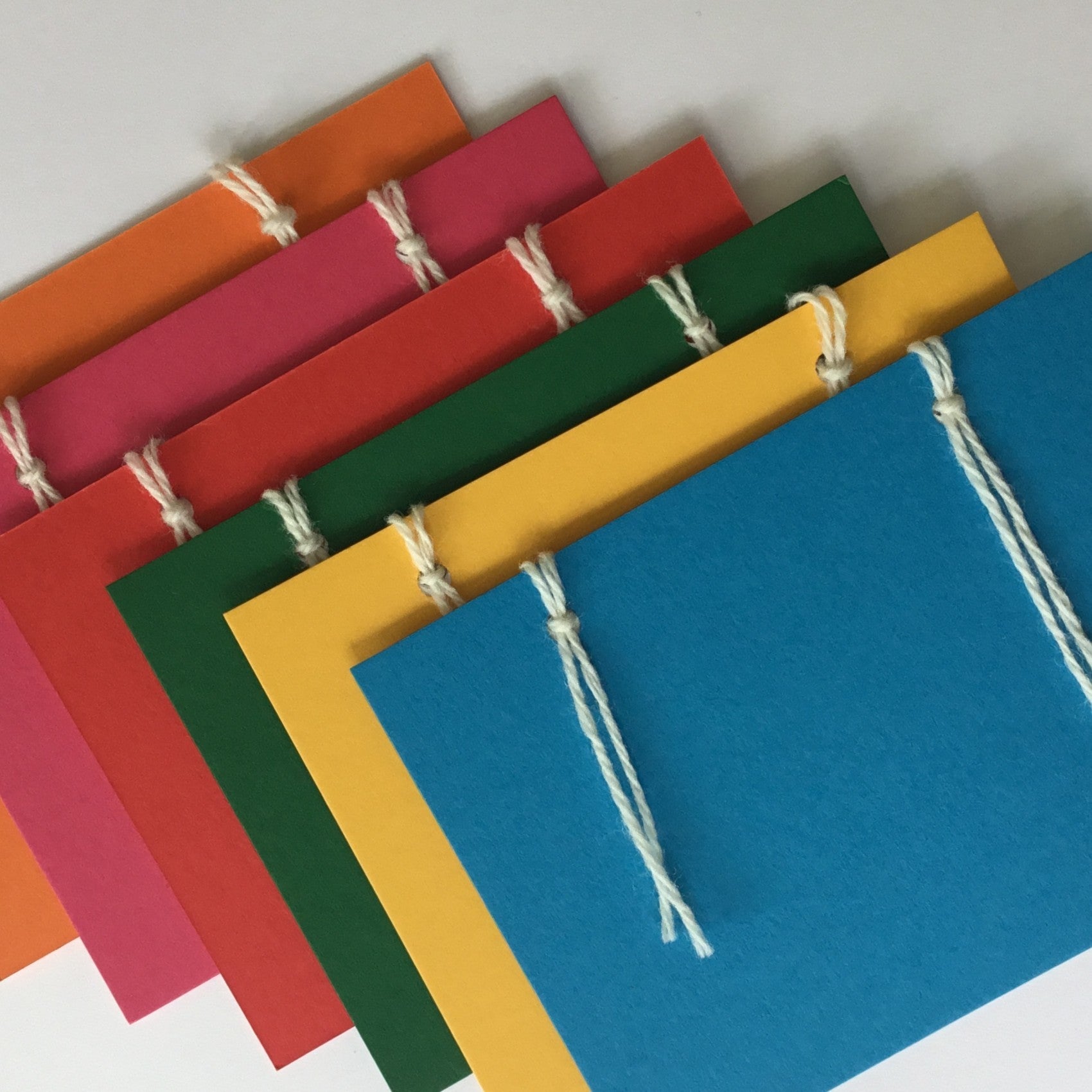 A set of 6 colour cards in: colours: blue, green, red, yellow, orange and pink. The back of the cards have 3 notepapers.  These are attached with 2 wool loops. The set has 6 envelopes included, they are not shown in the photo.