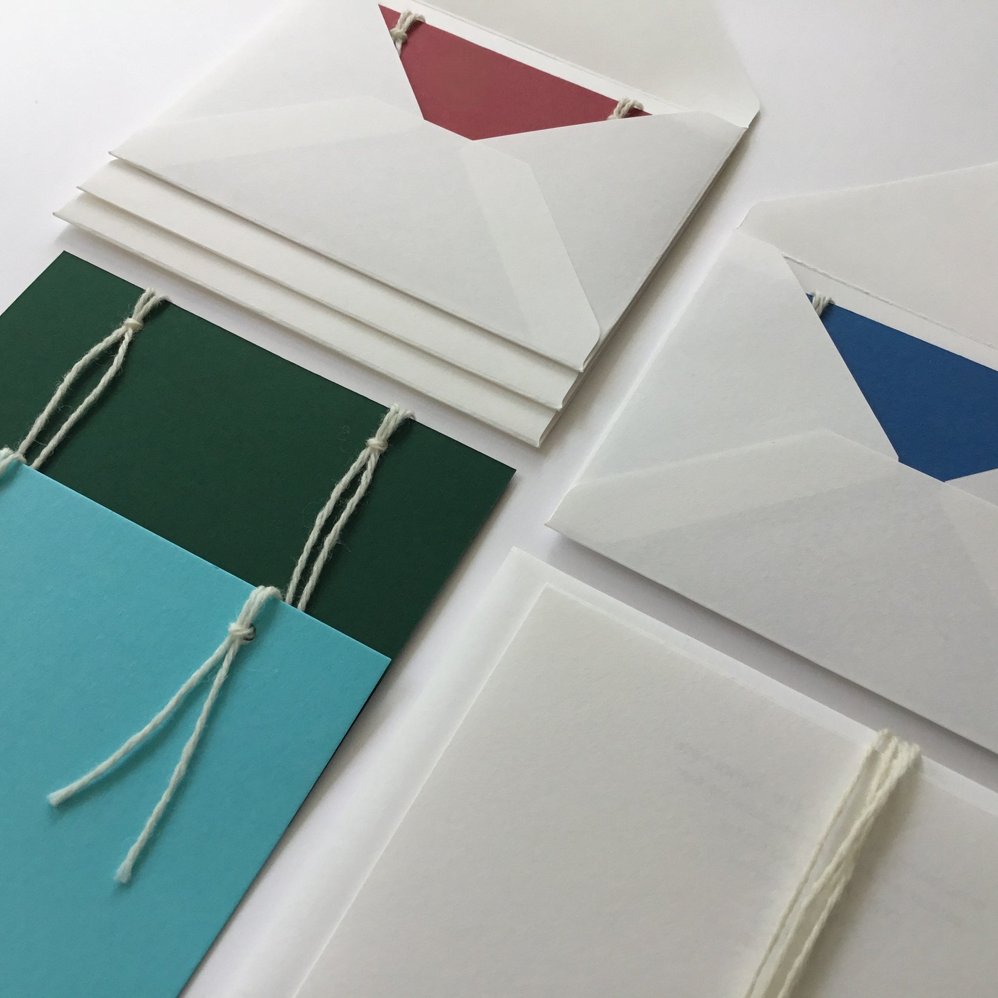 The reusable greeting card. A set of 4 handmade note cards in: 1 shade of green, 2 shades of blue and a deep red. The set has 4 handmade envelopes. One envelope is slipped under the wool of the gift pouch.  The back of the cards have 3 note papers.  These are attached with 2 wool loops.