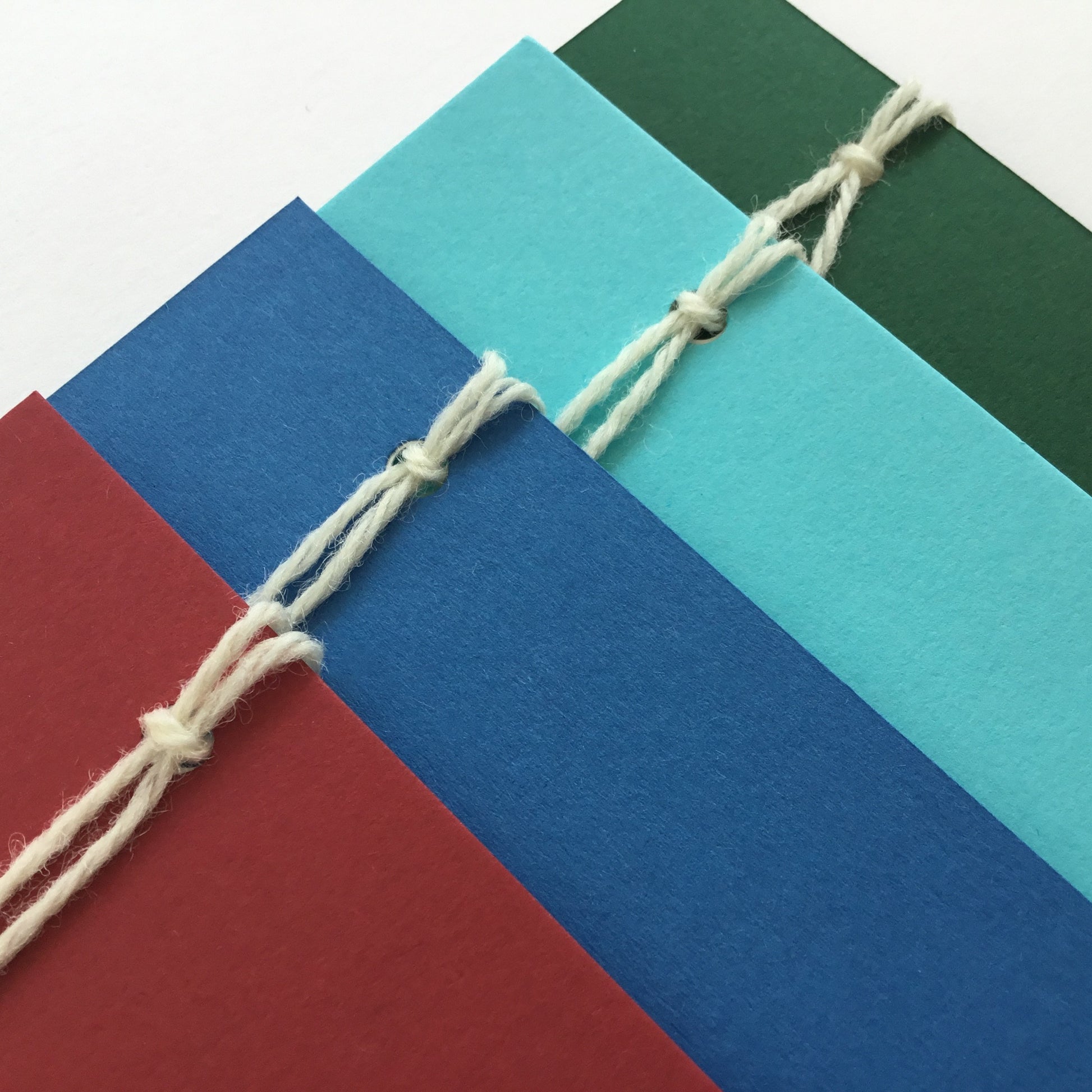 A set of 4 colour cards in: 1 shade of green, 2 shades of blue and a deep red. The set has 6 envelopes, not shown in the photo.  The back of the cards have 3 notepapers.  These are attached with 2 wool loops.