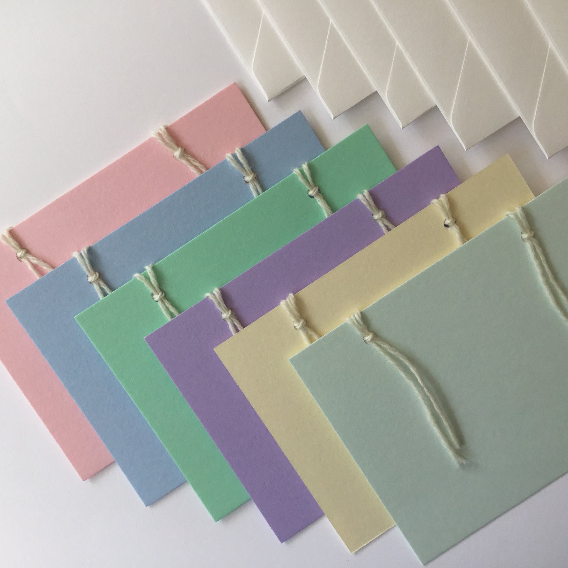The reusable greeting card. A set of 4 handcrafted cards in light  pastel colours: pink, blue, green, purple and yellow with 6  handcrafted envelopes. The back of the cards have 3 note papers.  These are attached with 2 wool loops.