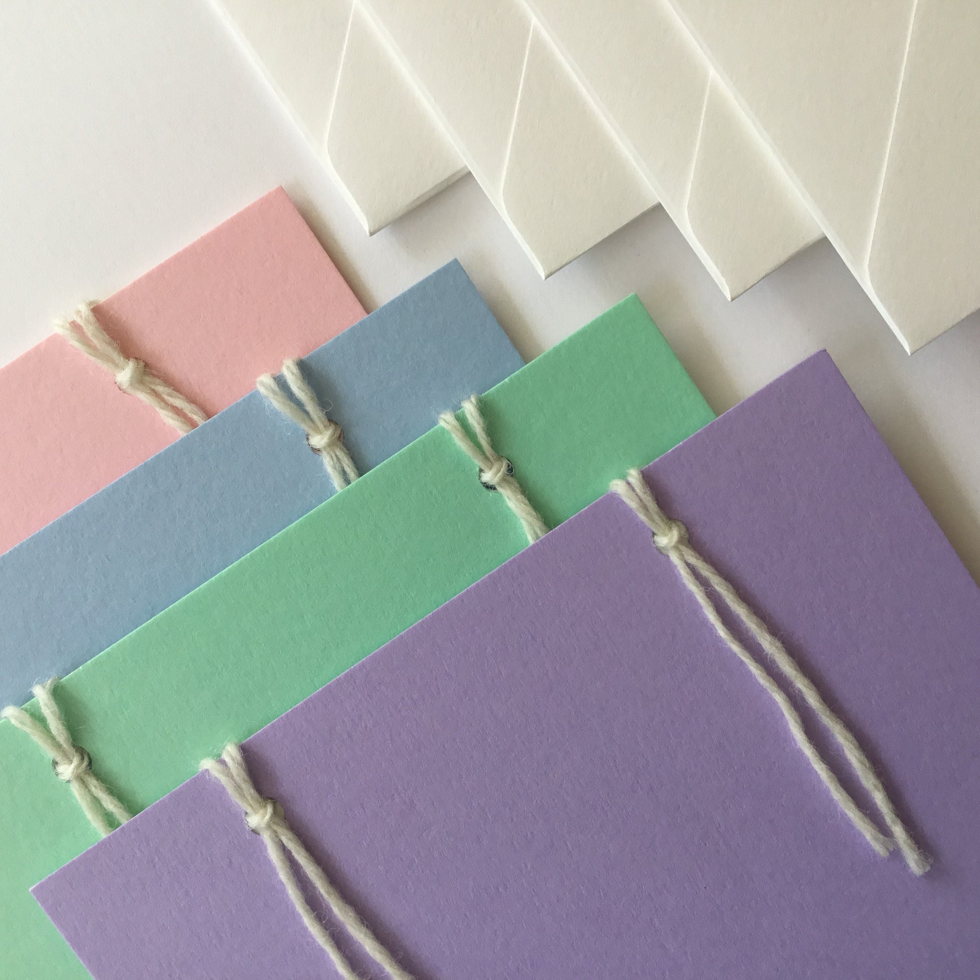 The reusable greeting card. A set of 4 handcrafted cards in light  pastel colours: pink, blue, green, purple and yellow with 4  handcrafted envelopes. The  back of the cards have 3 note papers.  These are attached with 2 wool loops.