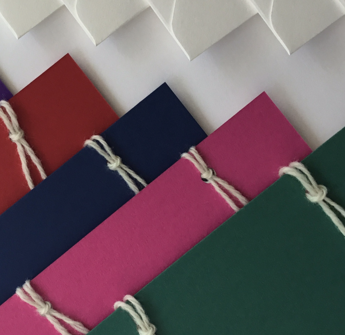 A set of 4 handmade colour cards in: green, pink, blue and red. The set has 4 handmade envelopes. The back of the cards have 3 notepapers.  These are attached with 2 wool loops.